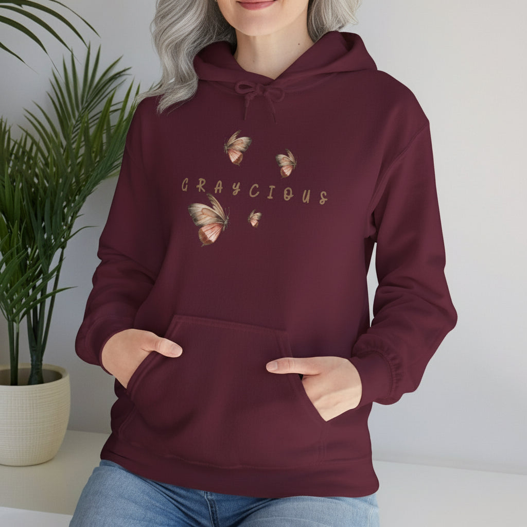 Person wearing a maroon hoodie with butterfly designs and 'GRACIOUS' text, standing indoors.